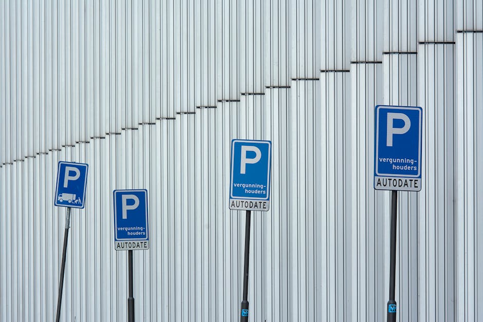 A vertical metal parking restriction sign mounted on a pole in front of a stone wall with a large window above. The top sign indicates no parking except with a permit from 7 am to 6 pm, Monday to Frid