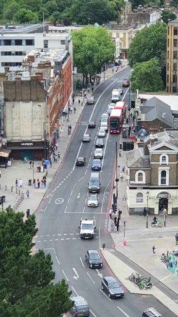 A daytime street scene in Charlton featuring a row of parked cars along the pavement in front of a historic building with a clock tower, which has a domed spire and arched windows, surrounded by tall